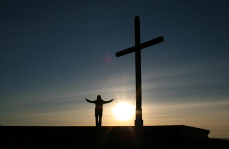 silhouette of person standing beside cross during sunset